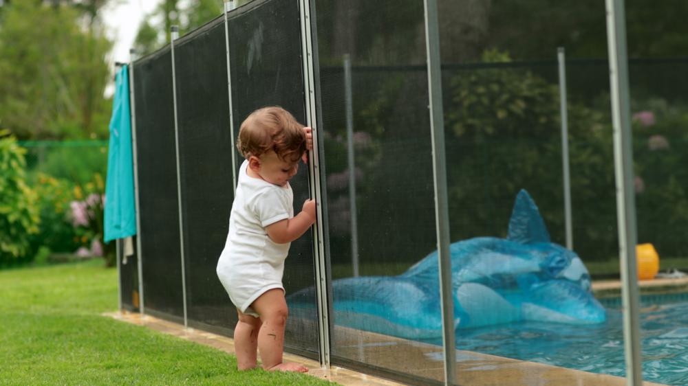 宝宝靠在游泳池栅栏保护。婴儿站在安全门